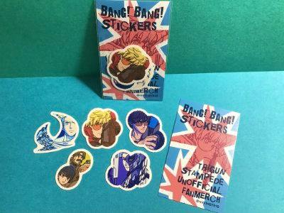 Several BANG! BANG! stickers arranged on a blue surface next to the product backing card.