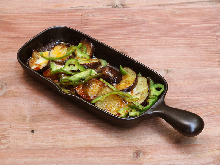 A rectangular ceramic grill plate with a handle containing cooked vegetables on a wooden surface.