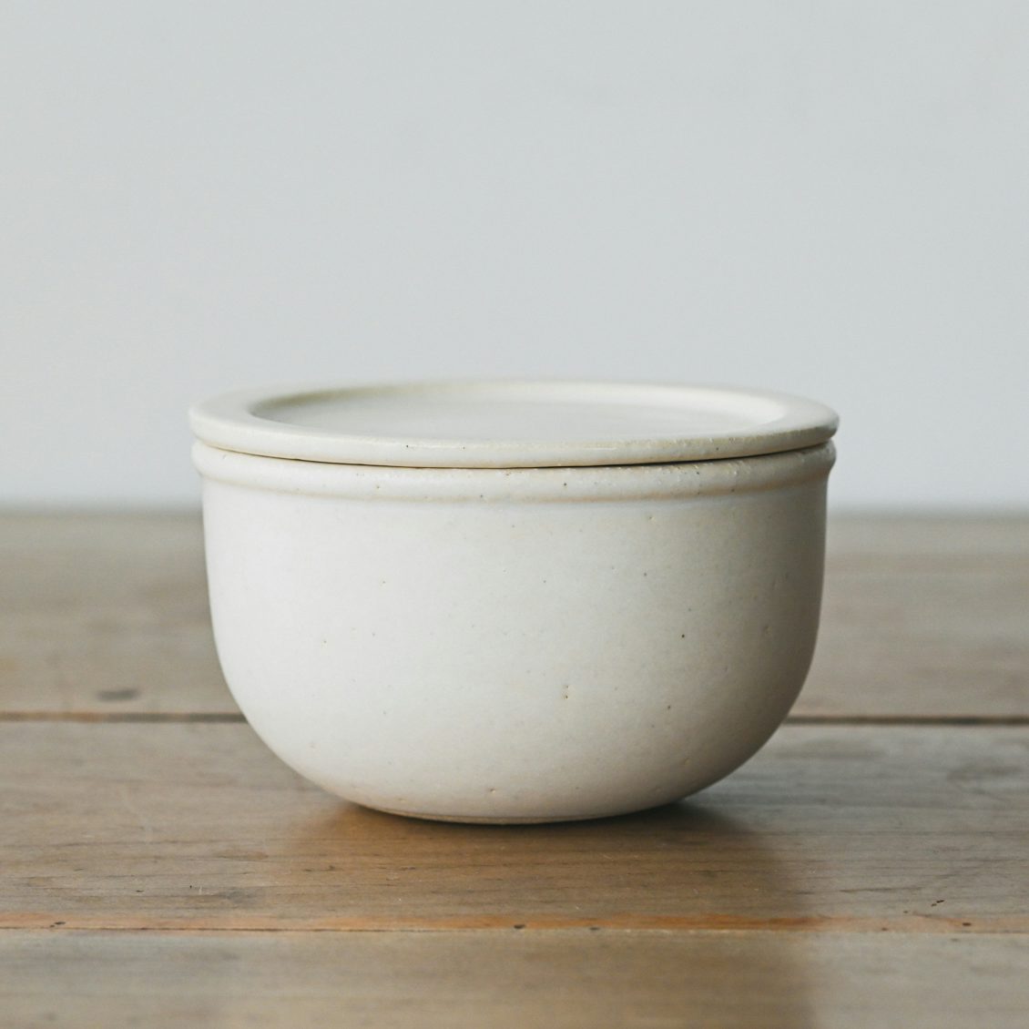 A small white Banko ware ceramic single-serving rice container with lid on a wooden surface.
