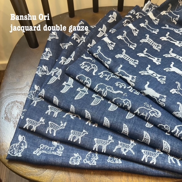 Folded dark blue Banshu ori jacquard double-gauze cotton fabric with white animal motifs displayed on a chair.