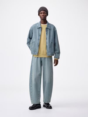 A model wearing light-blue barrel-leg men's jeans paired with a denim jacket.