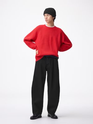 A person modeling the black barrel-leg jeans with a red sweater and black beanie on a white background.