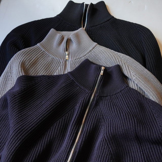 Three zip-up drivers knit jackets in sepia brown, beige, and black stacked flat.