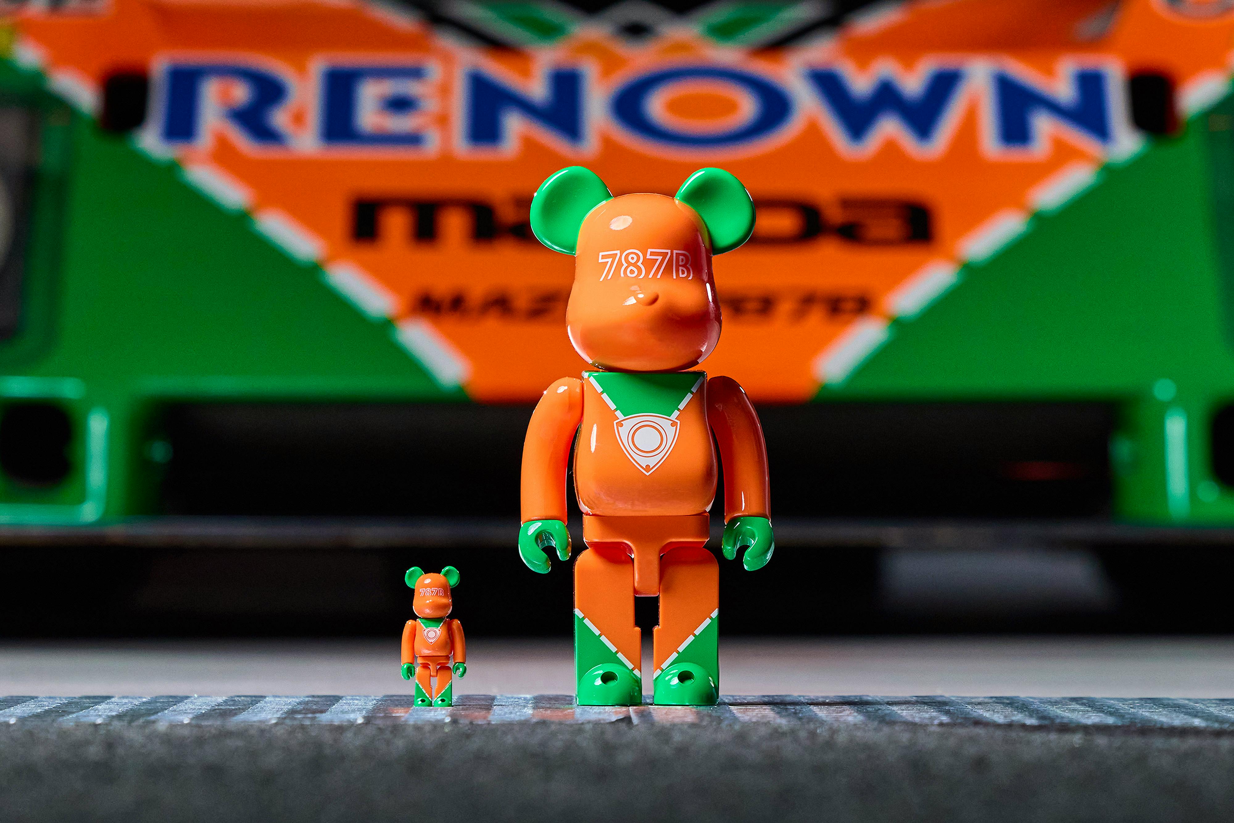Front view photo of two orange-and-green BE@RBRICK x MAZDA 787B figures with a blurred orange-and-green background.