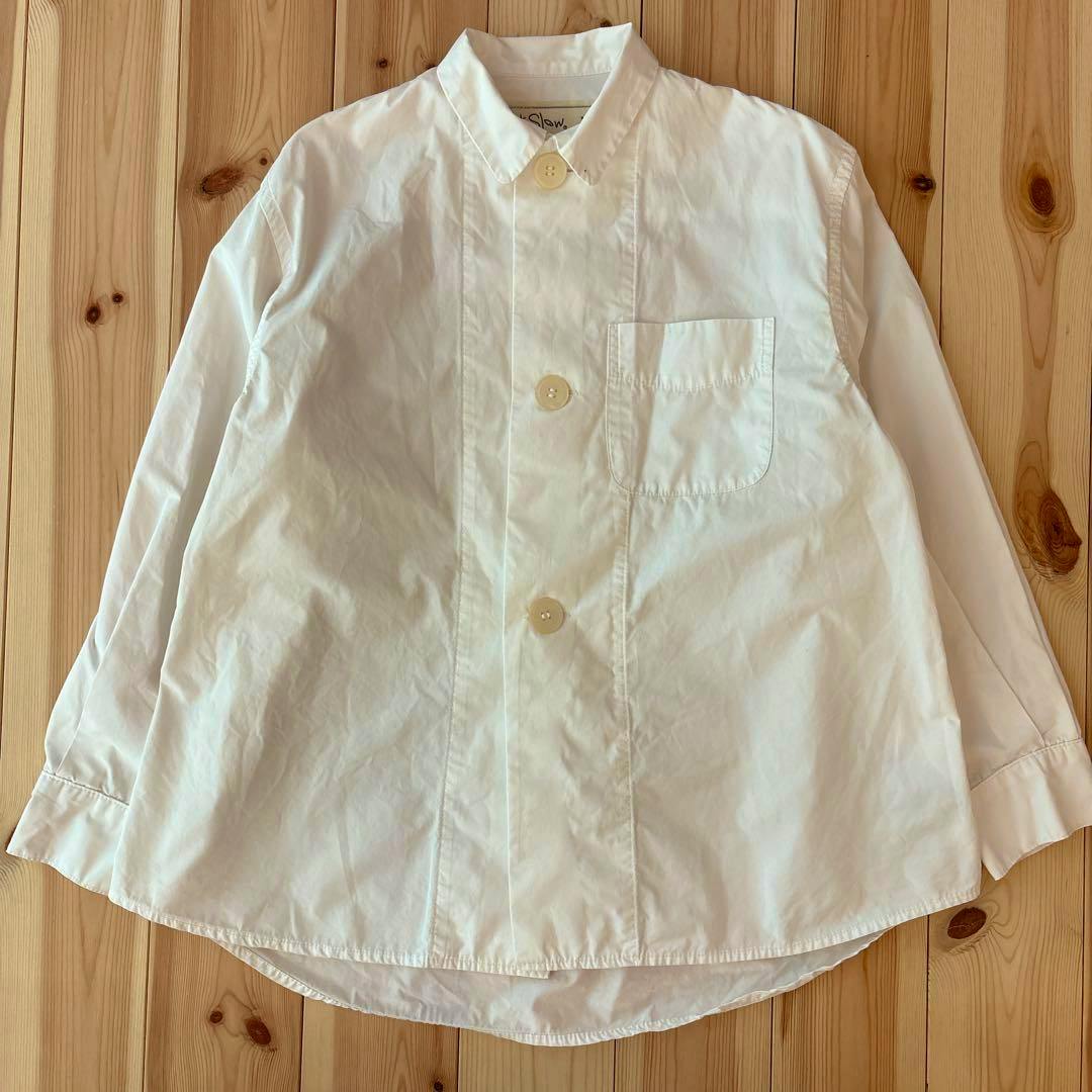 White men's cotton shirt jacket with large buttons and a chest pocket laid flat on a wooden floor.