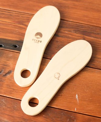 Two shoehorns pictured on a wooden surface, one showing a BEAMS logo.