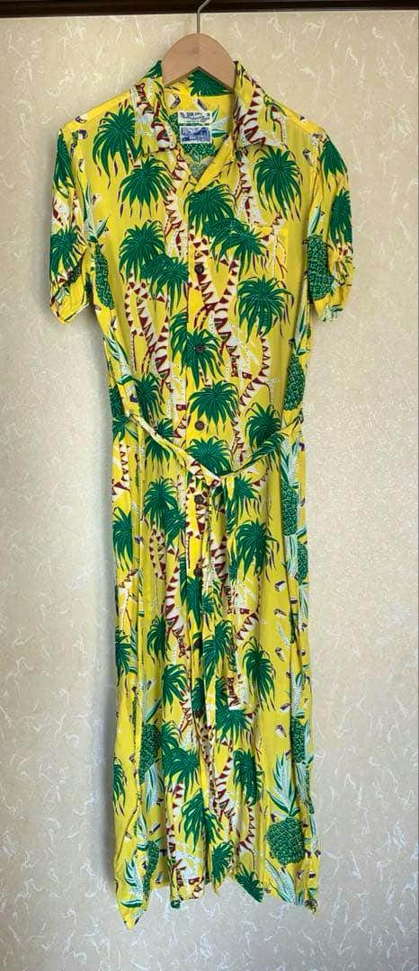 Front view of a yellow BEAMS long women's cotton dress with green pineapple and palm tree print hanging on a wooden hanger.