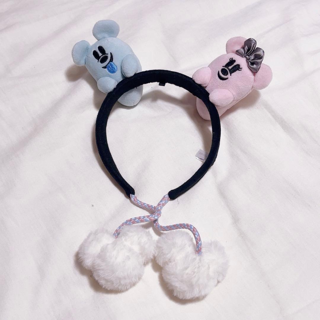 A black headband with blue and pink bear-ear plush decorations and two white pom-poms attached.