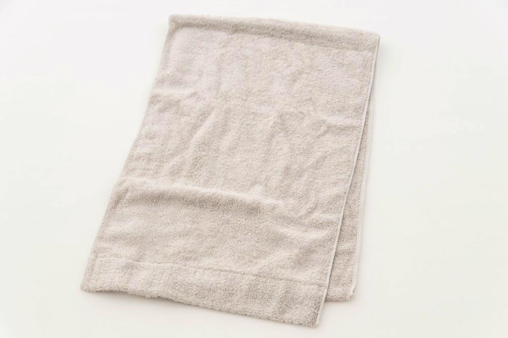 A light beige cotton bath towel folded and laid flat on a white background.