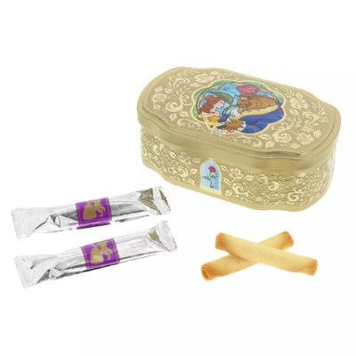 A gold decorative cookie tin featuring Beauty and the Beast artwork shown with two wrapped cookies and two unwrapped cookies.