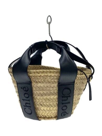 Beige woven straw shoulder bag with wide black leather straps showing "Chloé" branding, photographed hanging on a hook.