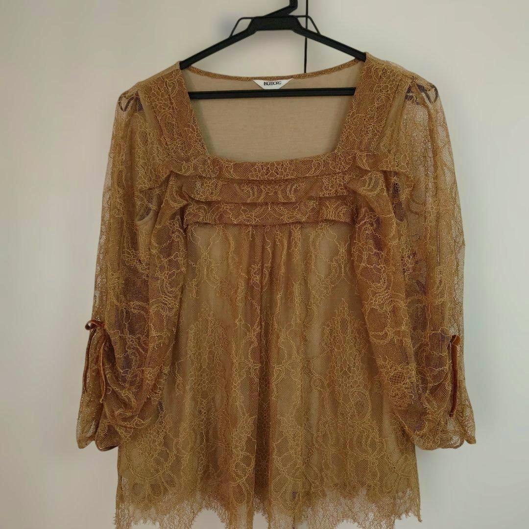Beige lace top hanging on a black hanger showing the front with a square neckline and three-quarter sleeves.