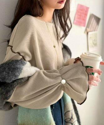 Model wearing a beige long-sleeve blouse with flared sleeves and a button detail, holding a takeaway cup.