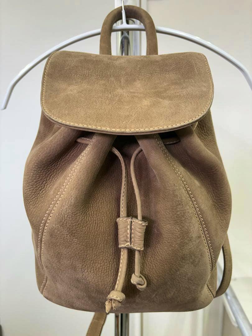 Front view of a beige suede drawstring backpack hanging on a metal rack.