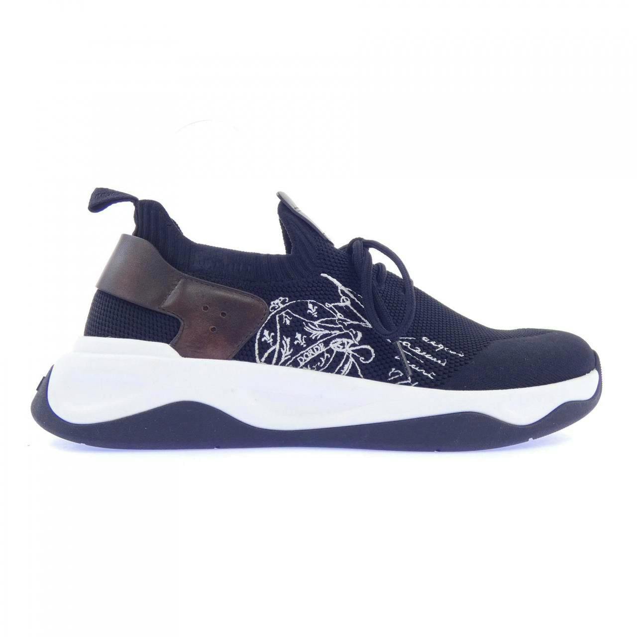 Side profile of a Berluti sneaker showing a dark knit upper, white sole, and a brown heel panel.