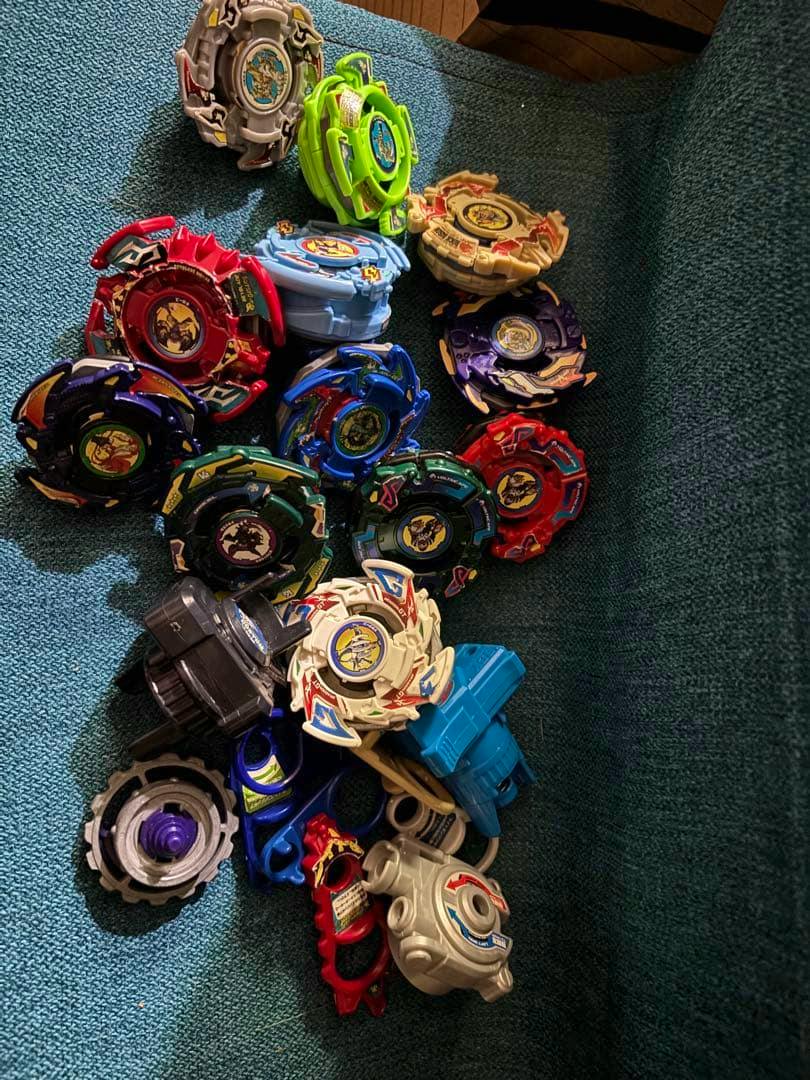 A large assortment of Beyblade toy tops and launchers arranged on a teal fabric surface.