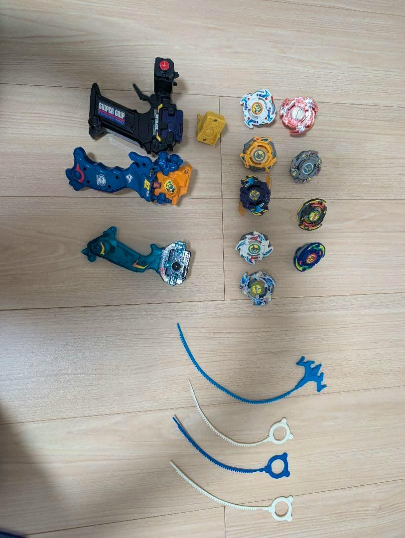 Several Beyblade tops with launchers, grips, and ripcords arranged on a wooden floor.