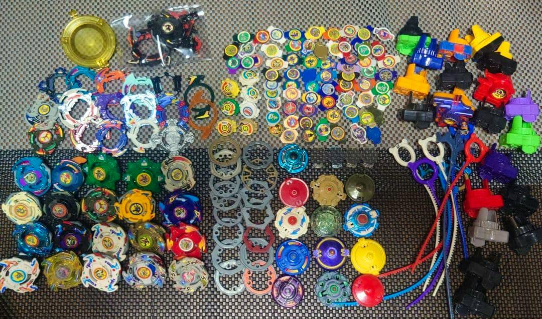 Assortment of Beyblade toy parts, tops, rings, and launchers arranged on a mat.