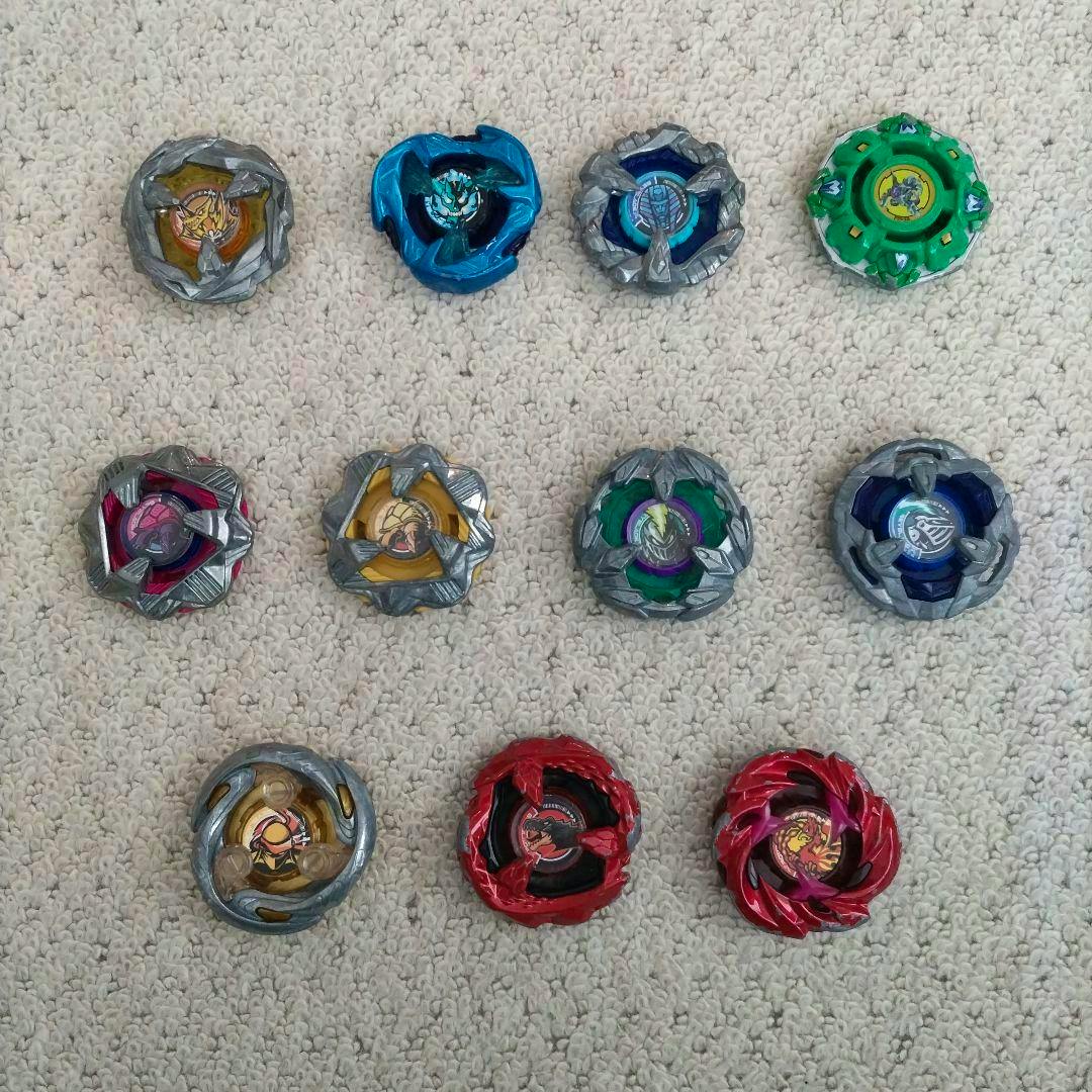 Multiple Beyblade custom parts and assembled tops arranged in rows on a carpet.