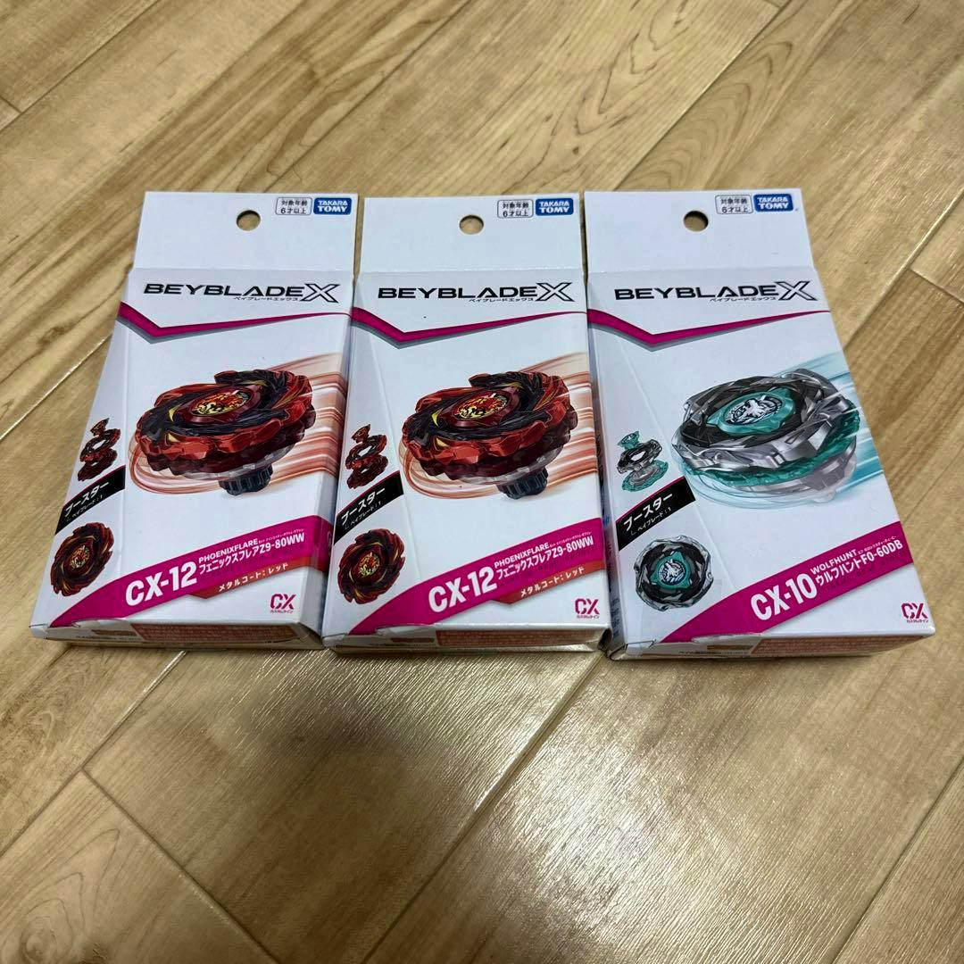 Three Beyblade X boxed toys (two labeled CX-12 and one labeled CX-10) arranged on a wooden floor.