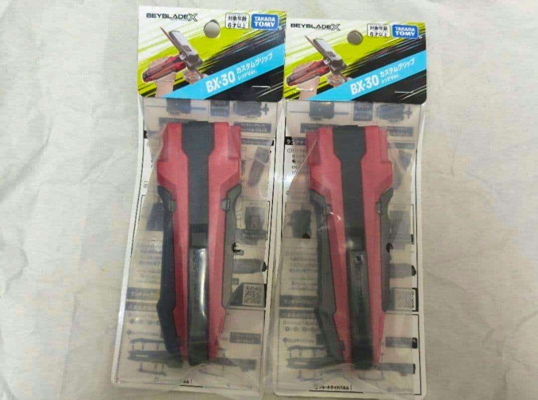 Two red BEYBLADE X BX-30 custom grips in clear retail blister packaging displayed side by side.