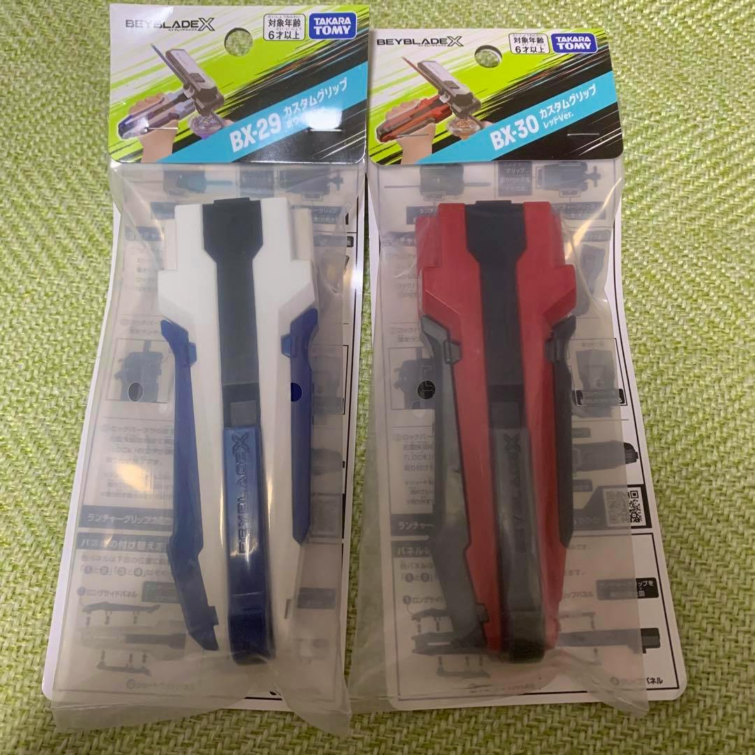Two Beyblade X custom grips (BX-29 and BX-30) shown side by side in their retail packaging.