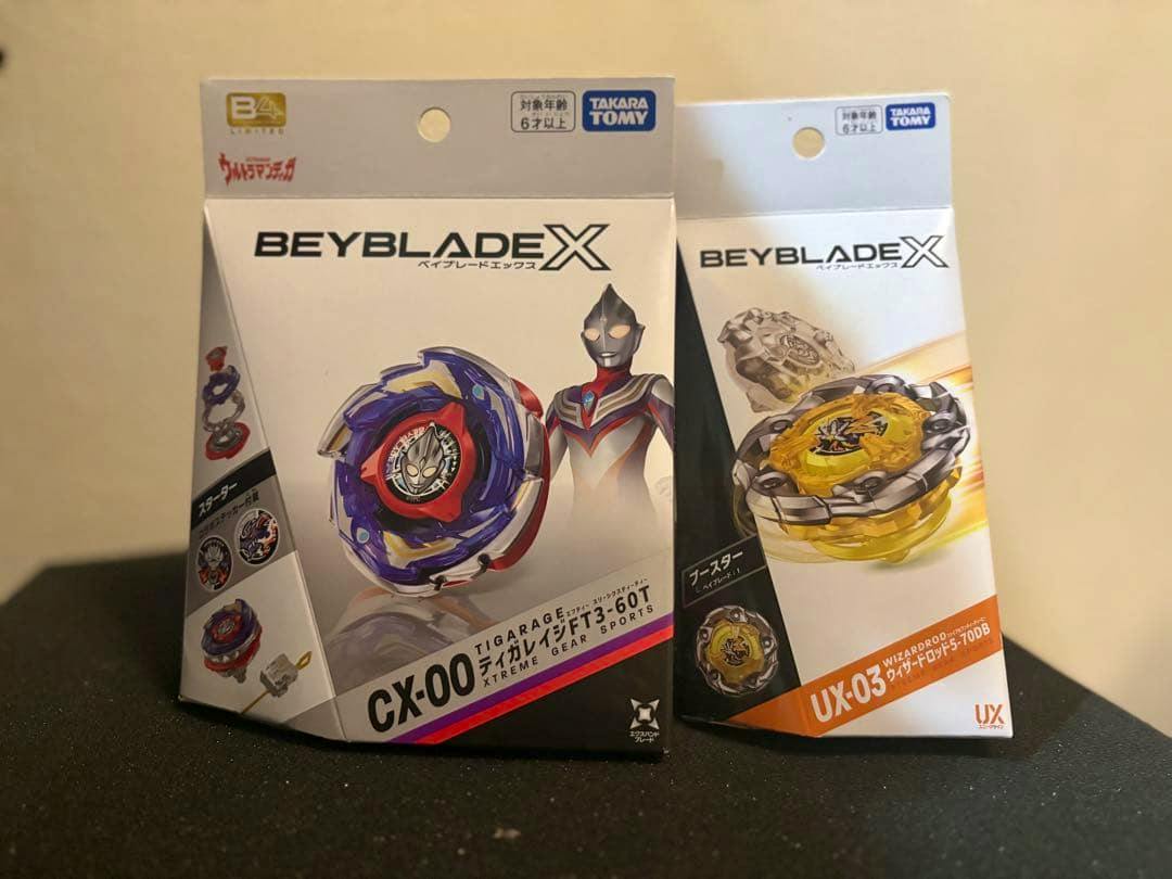 Two boxed Beyblade X toy packages labeled CX-00 and UX-03 displayed side by side on a surface.