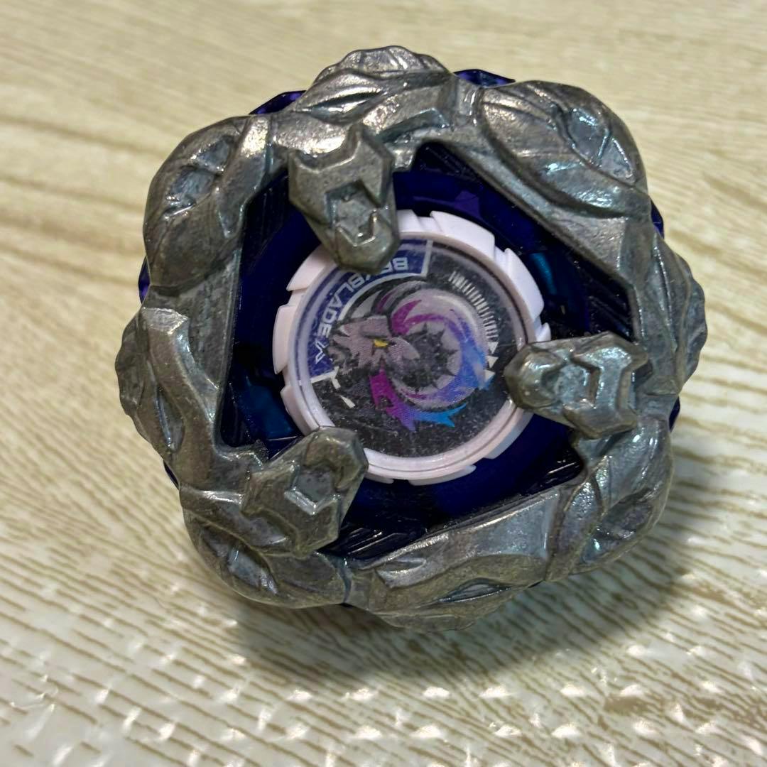 Close-up of the Beyblade toy top showing a silver metal outer ring and the central emblem sticker.