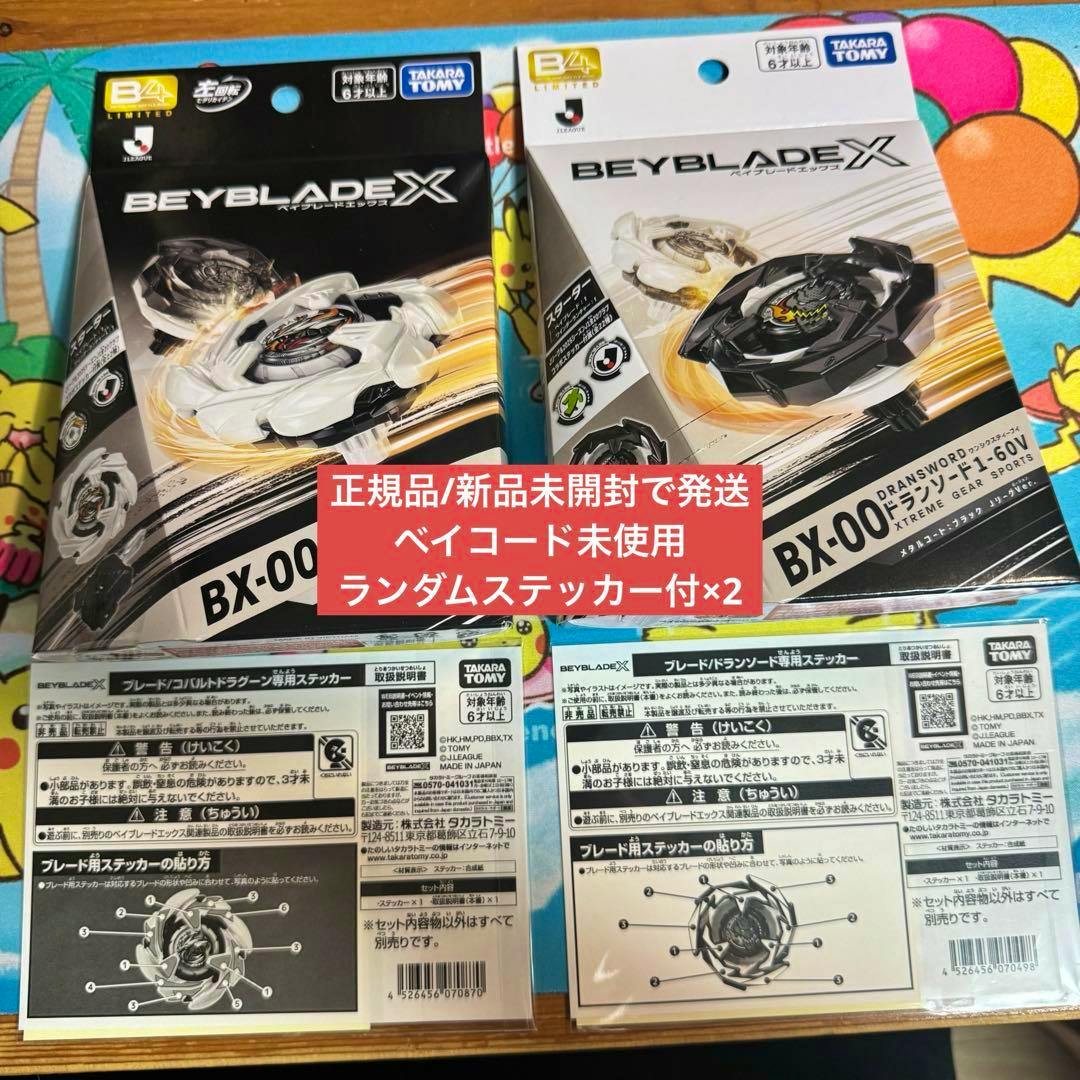 Photograph of two Beyblade X BX-00 product boxes (Dransword/Cobalt Dragoon) with sticker sheets displayed below.