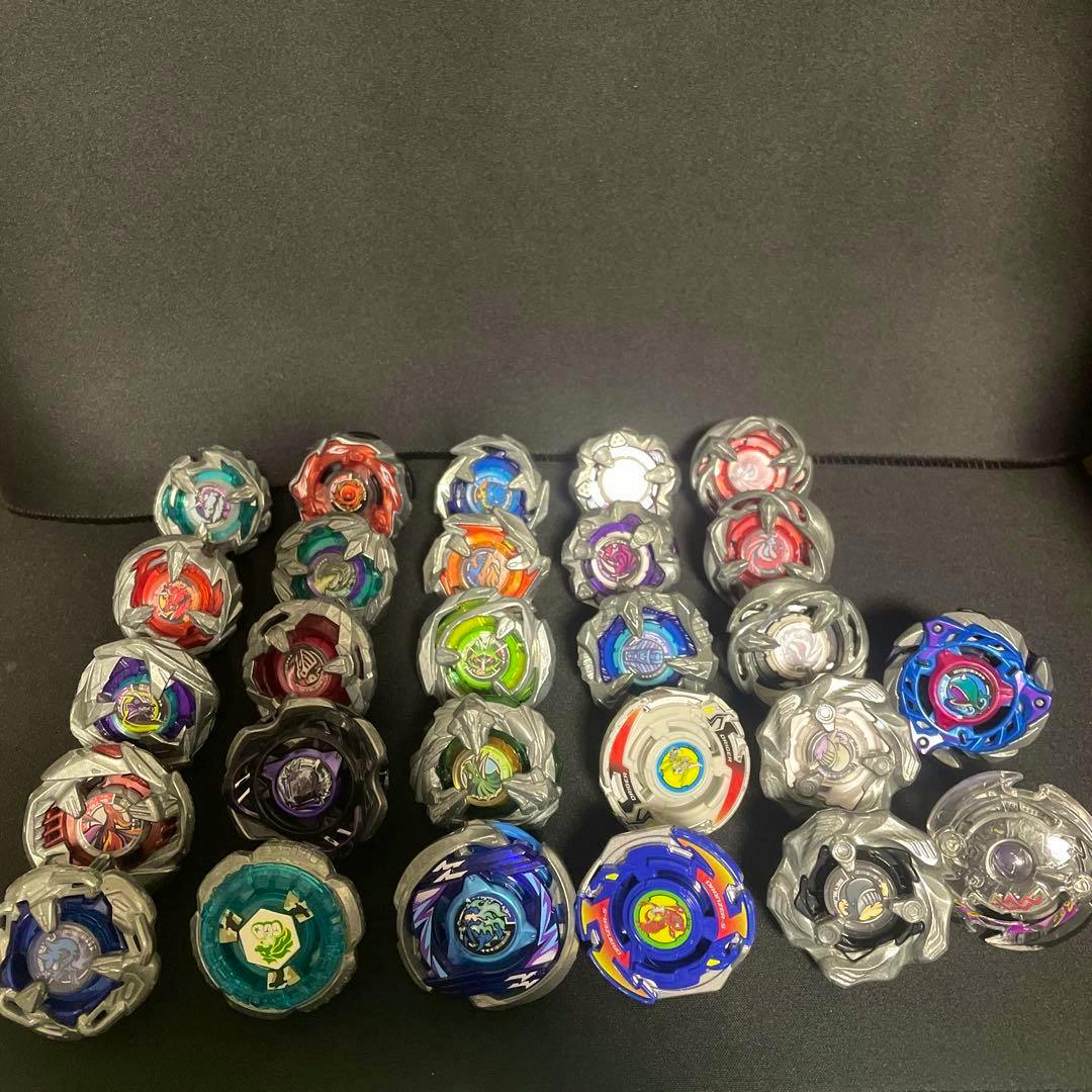 A set of BEYBLADE X spinning tops (27 pieces) arranged in rows on a black surface.