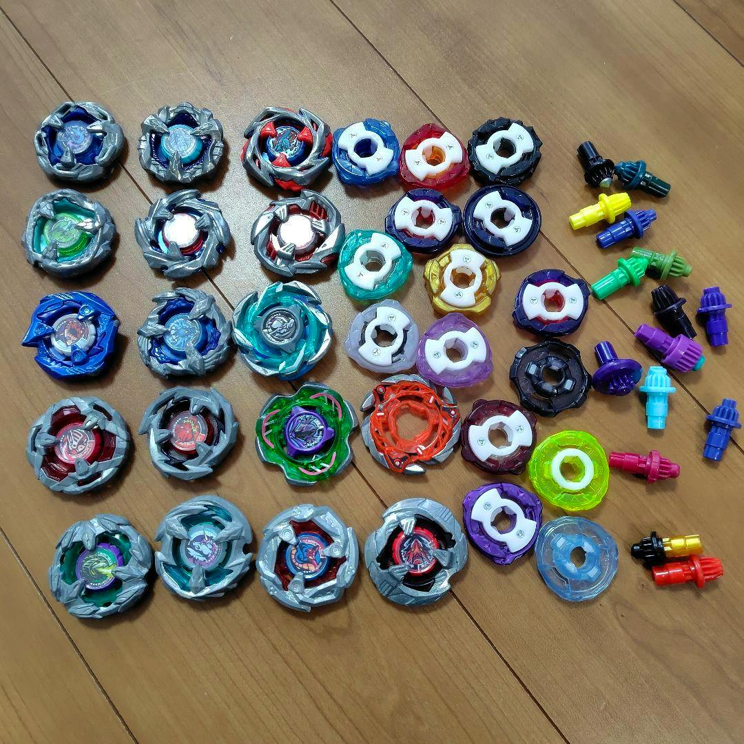 Several Beyblade X plastic tops and assorted parts laid out on a wooden floor.
