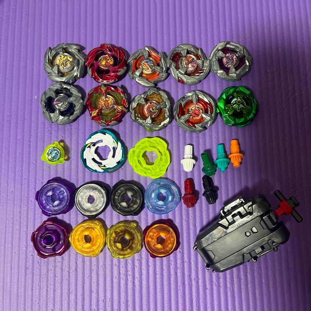 Multiple Beyblade X tops, assorted parts, and a launcher arranged on a purple mat.