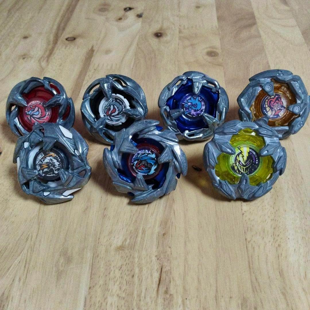 Seven Beyblade X spinning tops arranged on a wooden surface.