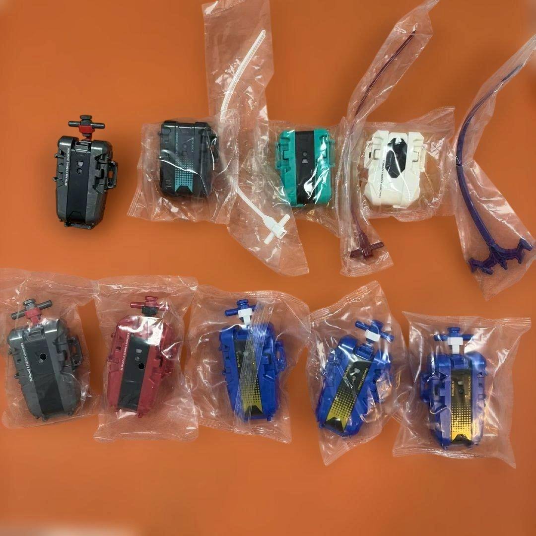 Multiple Beyblade X string launchers in individual plastic bags laid out on an orange background.