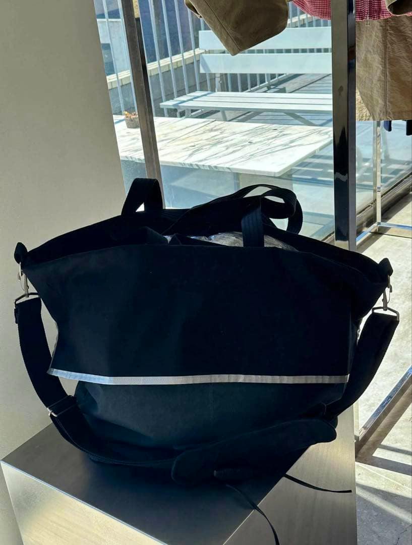 Black BIBLIOTHERK rain tote bag with a reflective strip and shoulder strap on a display surface.