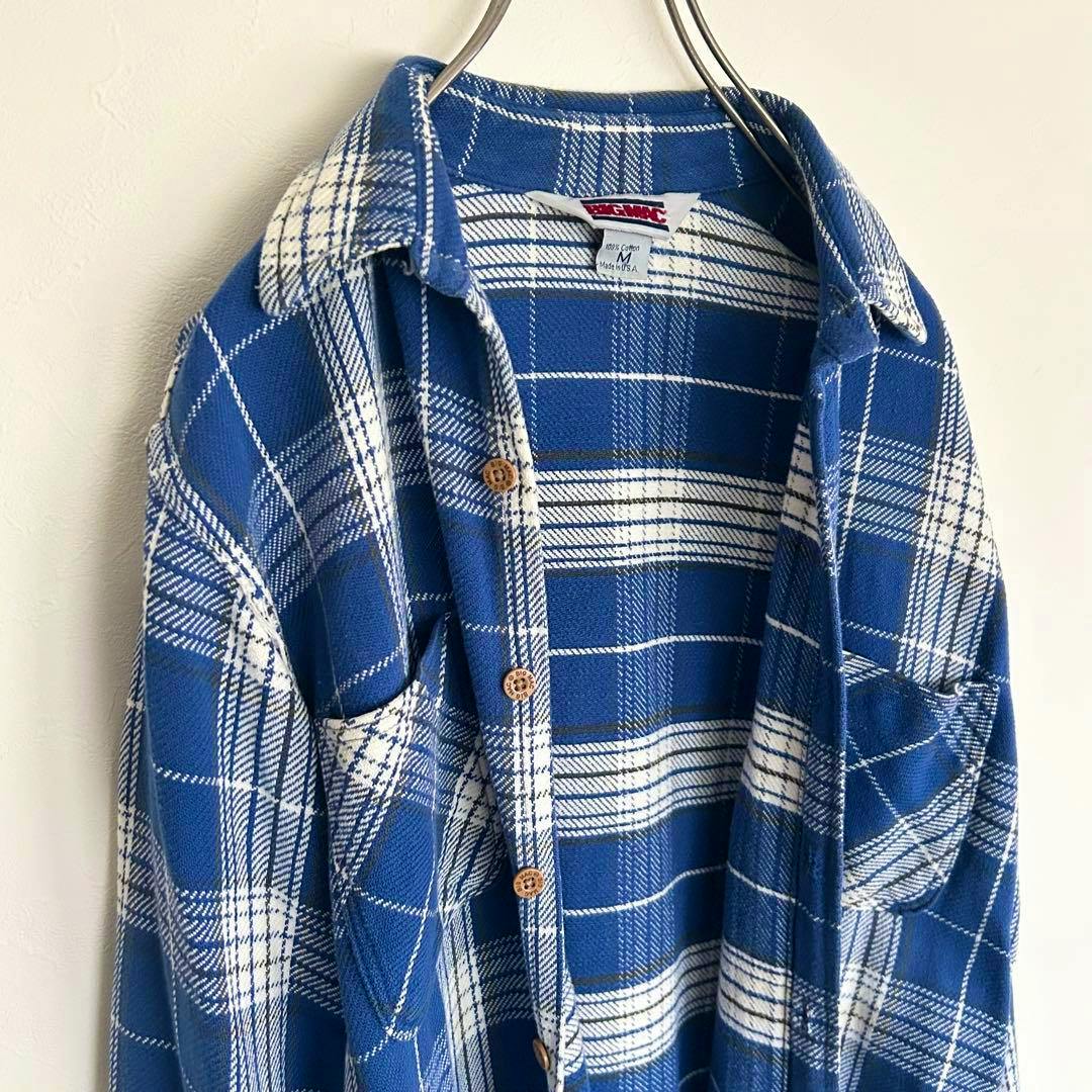 Blue and white plaid men's cotton flannel shirt hanging on a hanger showing the front, collar, buttons, and chest pockets.