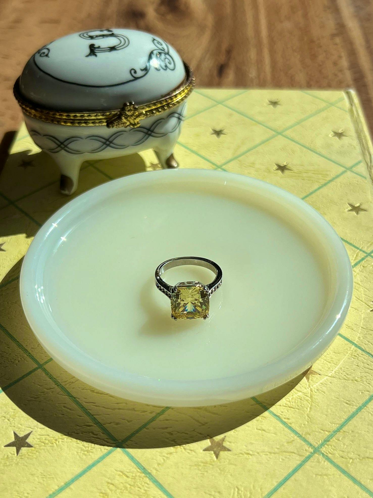 A ring with a large yellow square stone set in a metal band displayed on a white dish.