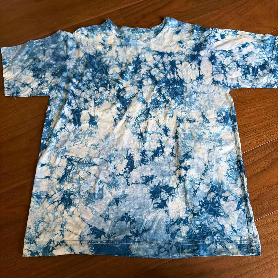 Front view of a blue indigo-style tie-dye cotton T-shirt laid flat on a wooden floor.
