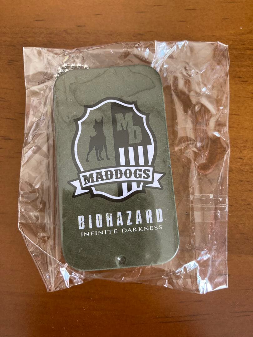 Front view of the BIOHAZARD Infinite Darkness steel can with a MADDOGS emblem, in clear plastic packaging on a wooden surface.