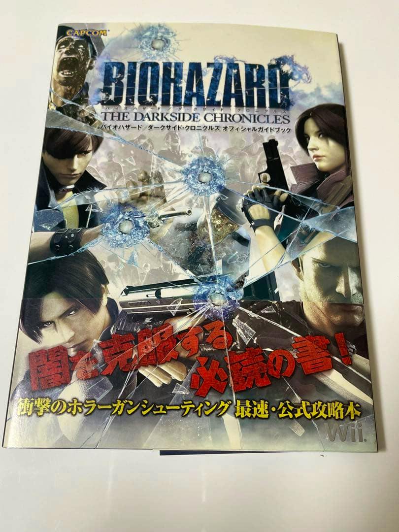 Front cover of the Biohazard: The Darkside Chronicles official guide book showing the title, character artwork, and a red Japanese promotional band at the bottom.