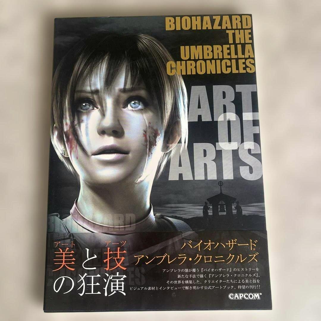 Front cover of the book showing a close-up of a character's face and the title "BIOHAZARD THE UMBRELLA CHRONICLES ART OF ARTS" with Japanese text at the bottom.
