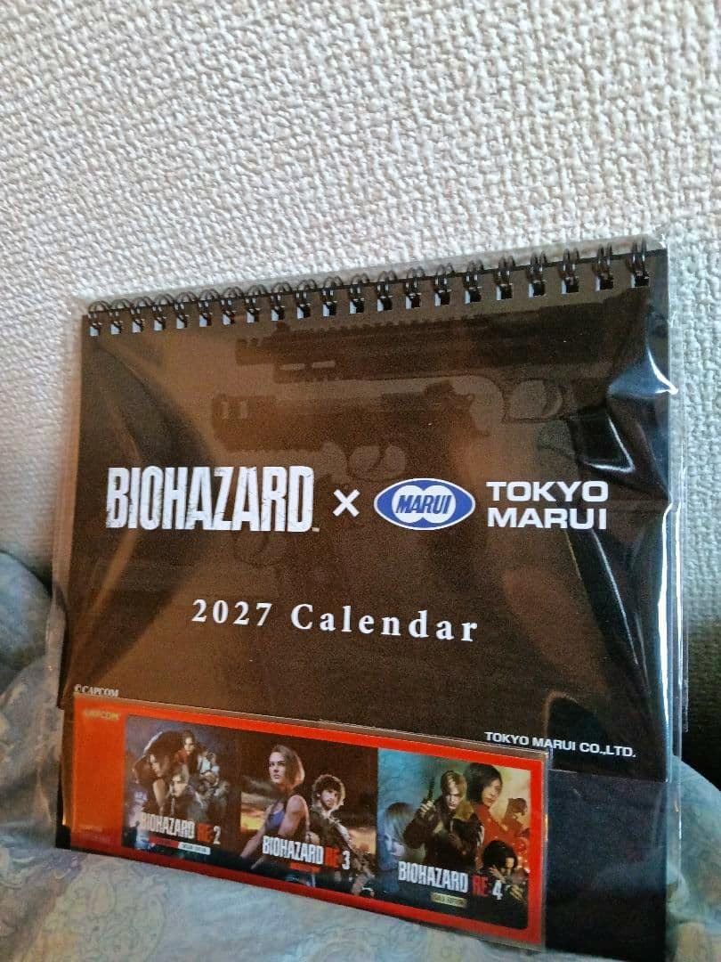 Front cover of the BIOHAZARD × TOKYO MARUI 2027 desk calendar in plastic packaging, showing the logos, '2027 Calendar' text, and small preview images.