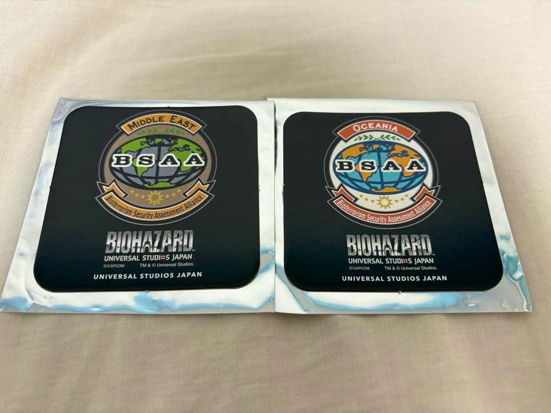 Two BIOHAZARD Universal Studios Japan paper coasters with BSAA logos in individual packaging placed on a beige surface.