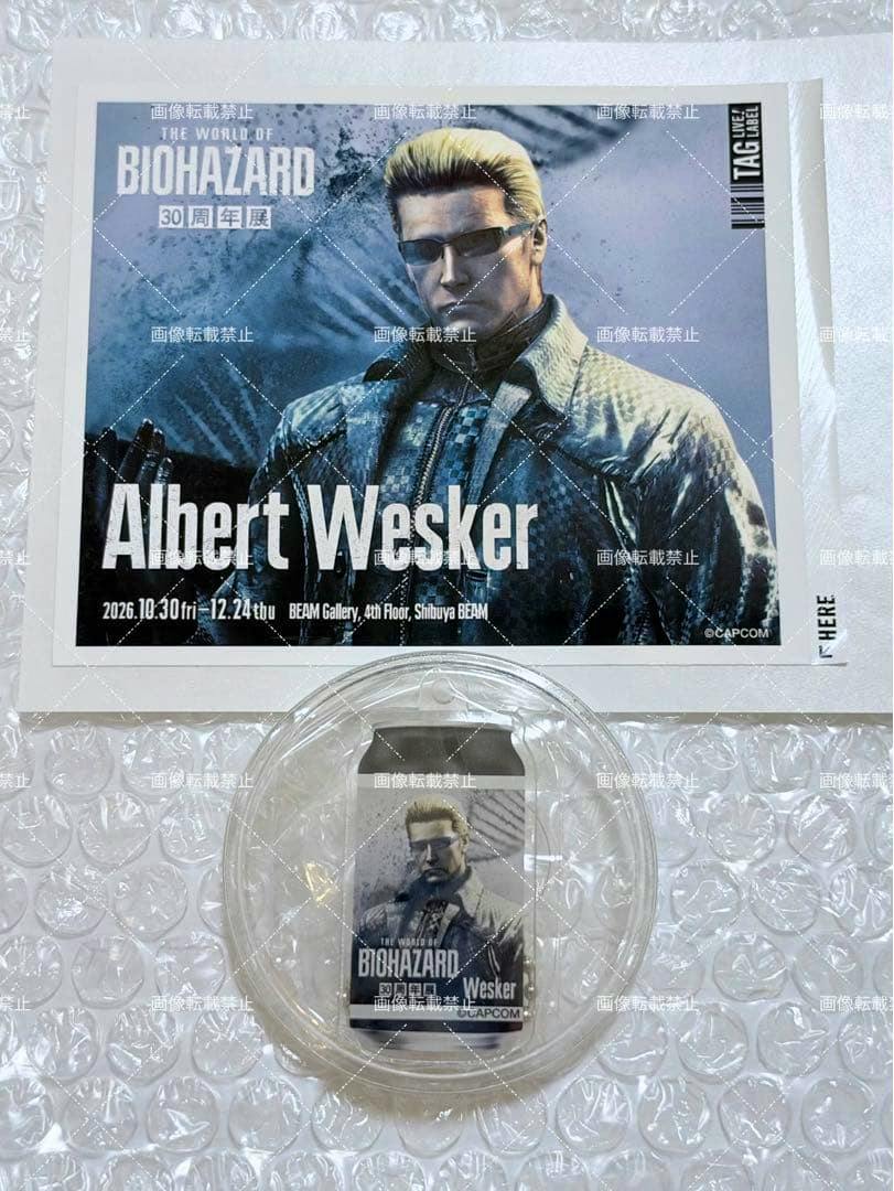 A small can-shaped BIOHAZARD Albert Wesker label can in a clear plastic capsule shown below an Albert Wesker printed card on bubble wrap.