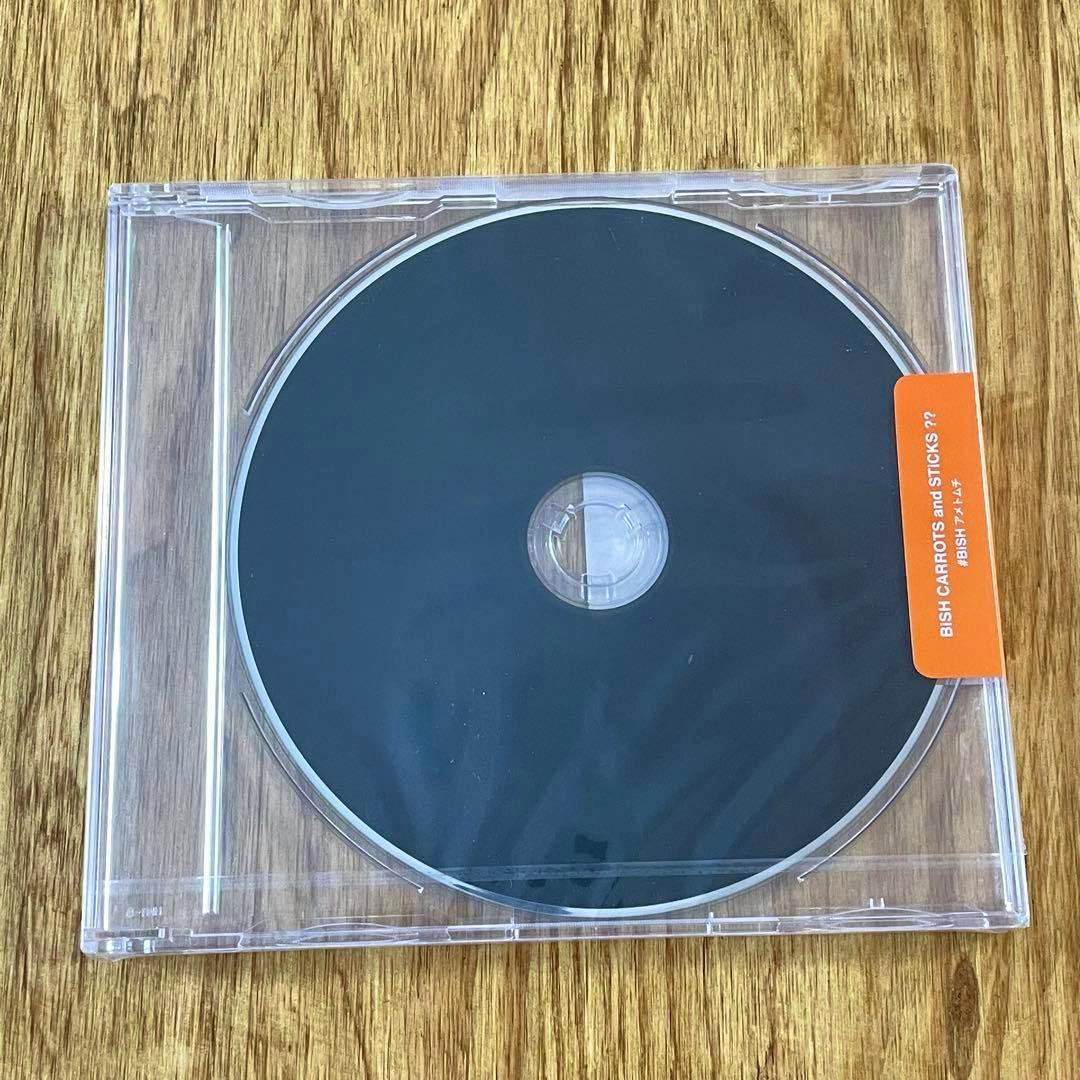 A CD in a clear jewel case showing a plain black disc and an orange label reading "BiSH CARROTS and STiCKS??" on a wood surface.