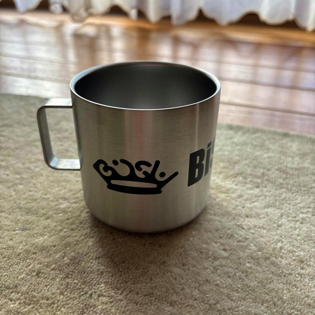 A stainless steel 380ml thermal mug with a handle showing a black crown graphic and partial "BiSH" text on a carpet.