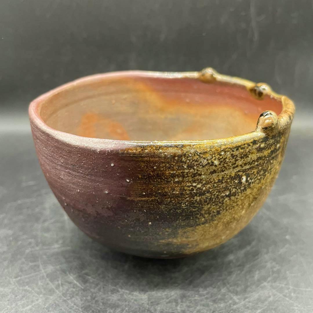 Bizen-yaki matcha tea bowl with brown and yellow glaze and three small nodules on the rim shown against a neutral background.