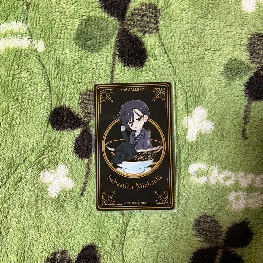 Photocard of Sebastian Michaelis featuring a chibi illustration on a black decorative card placed on a green blanket.