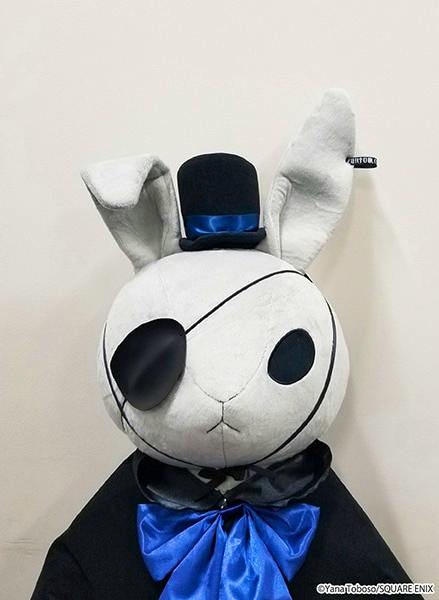 Front view of the "黒執事 Black Label" Big Bitter Rabbit plush wearing a small top hat, an eyepatch, and a blue bow against a plain light background.