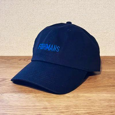 Black cotton baseball-style cap with blue embroidered text on the front, photographed on a wooden surface.